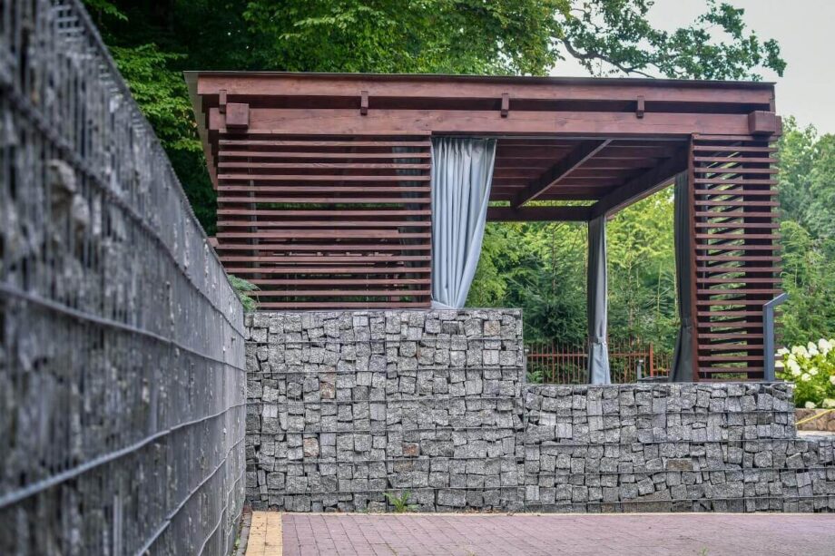 Ein Pavillon mit Holzterrassenlamellen und steinernen Wänden im Garten.