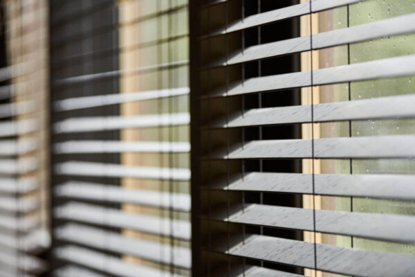 Ein Fenster zeigt ein System aus beweglichen Holzlamellen, die Licht regulieren.