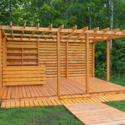 Eine offene Holzkonstruktion mit Holzlamellen steht im Grünen.