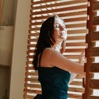 Eine Frau steht lächelnd vor einem Fenster mit der Entwicklung von beweglichen Holzlamellen.