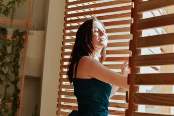 Eine Frau steht lächelnd vor einem Fenster mit der Entwicklung von beweglichen Holzlamellen.