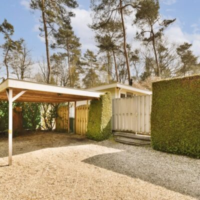 Ein Carport im Garten mit beweglichen Holzlamellen für Pergolen im Hintergrund.