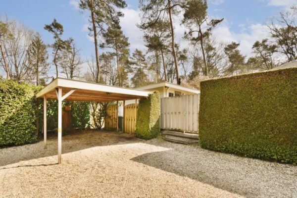 Ein Carport im Garten mit beweglichen Holzlamellen für Pergolen im Hintergrund.