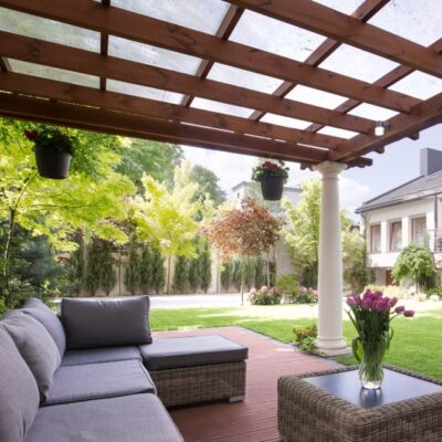 Unter einer Überdachung mit beweglichen Holzlamellen für den Garten steht eine moderne Sitzecke.