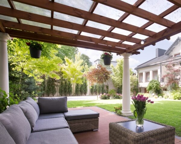 Unter einer Überdachung mit beweglichen Holzlamellen für den Garten steht eine moderne Sitzecke.