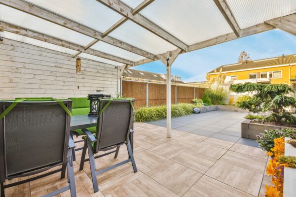 Überdachte Terrasse mit beweglichen Holzlamellen für den Garten im Hintergrund.