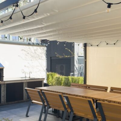Unter der Markise befinden sich eine lange Tafel und Stühle mit Holzterrassenlamellen.