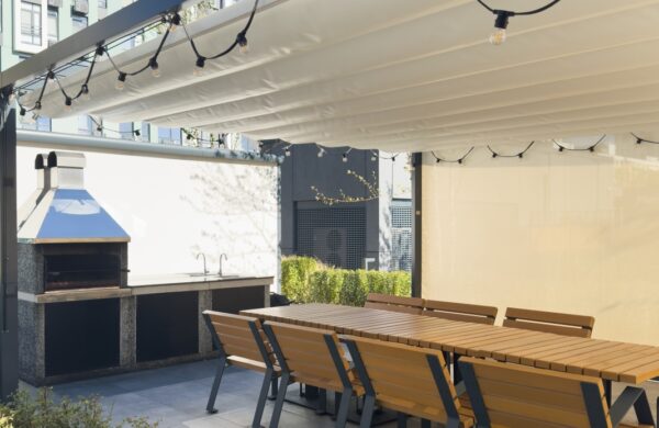 Unter der Markise befinden sich eine lange Tafel und Stühle mit Holzterrassenlamellen.