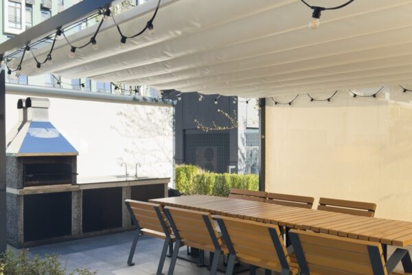 Unter der Markise befinden sich eine lange Tafel und Stühle mit Holzterrassenlamellen.
